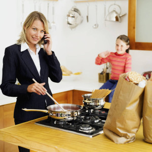 mother talking on a mobile phone while cooking with her daughter