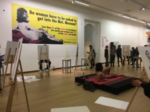 The live model drawing session. The male model posing as the nude in the Guerrilla Girls poster from 2012, shown in the background