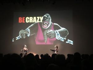 Presentation of the Guerilla Girls: Picture of a female gorilla in a pink bathing suit, with the wrods "Be crazy" written on the picture